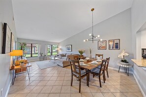 Un vaste espace de vie comprenant une table à manger pour six personnes, un canapé et une table basse. Une grande fenêtre offre une belle vue sur l’extérieur et permet à la lumière naturelle d’entrer.