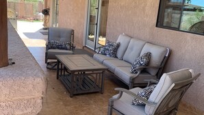Ein überdachter Patio-Bereich mit einer Couch, Sesseln und einem Tisch.