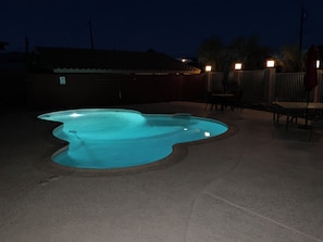 A swimming pool with a wavy edge design, surrounded by a fenced patio area with outdoor seating.