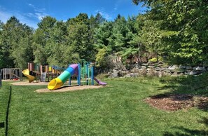 Explore the playground area with slides and climbing elements surrounded by lush trees and a stone wall.