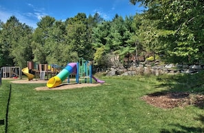 Explore the playground area with slides and climbing elements surrounded by lush trees and a stone wall.