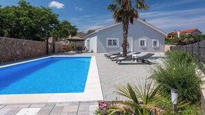 A swimming pool area with lounge chairs, a palm tree, and a stone wall. - Villa Mia with pool in Garica (Garica)