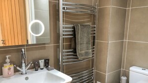 A bathroom with a white sink, a mirror with a light, a towel rack, and a toilet. - The Hideaway (St Ives)
