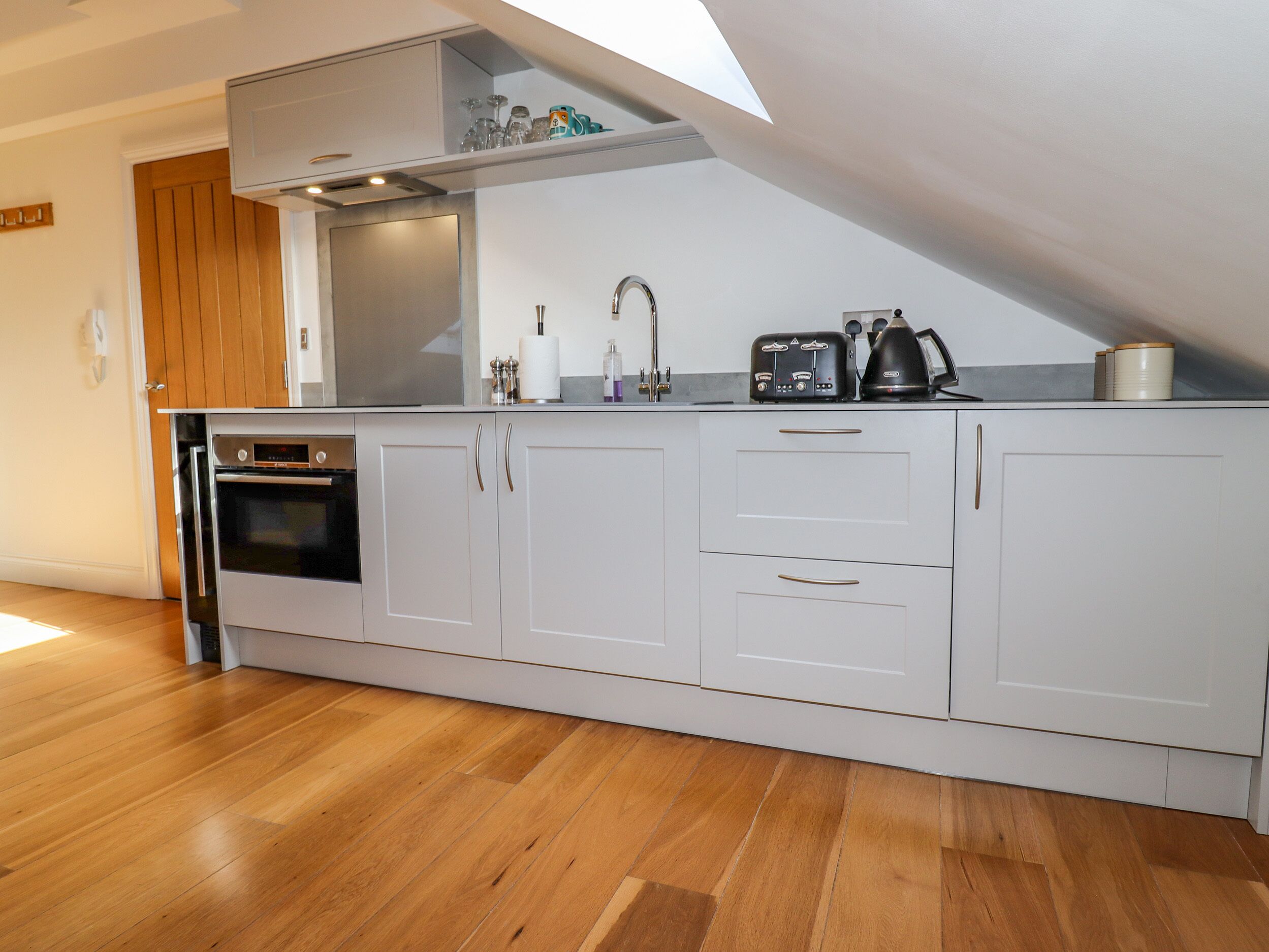 Een moderne keuken met witte kastjes, een inbouwoven, een broodrooster en een waterkoker.