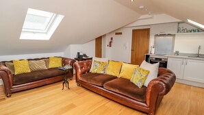 A spacious loft with a high ceiling, a large brown leather sofa, a small side table, and a skylight. - The Hideaway (St Ives)