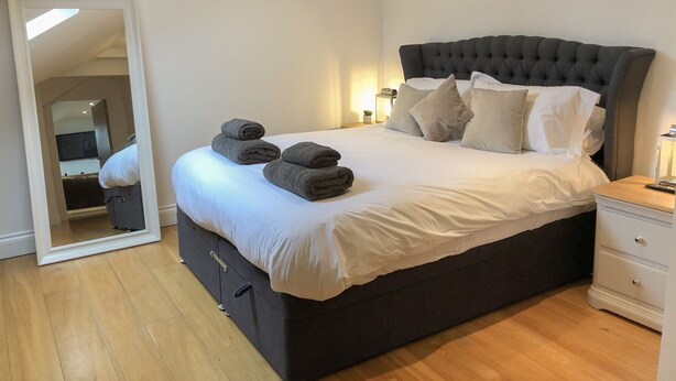 A bedroom with a large bed, a dark headboard, and a bedside table with a lamp. - The Hideaway (St Ives)