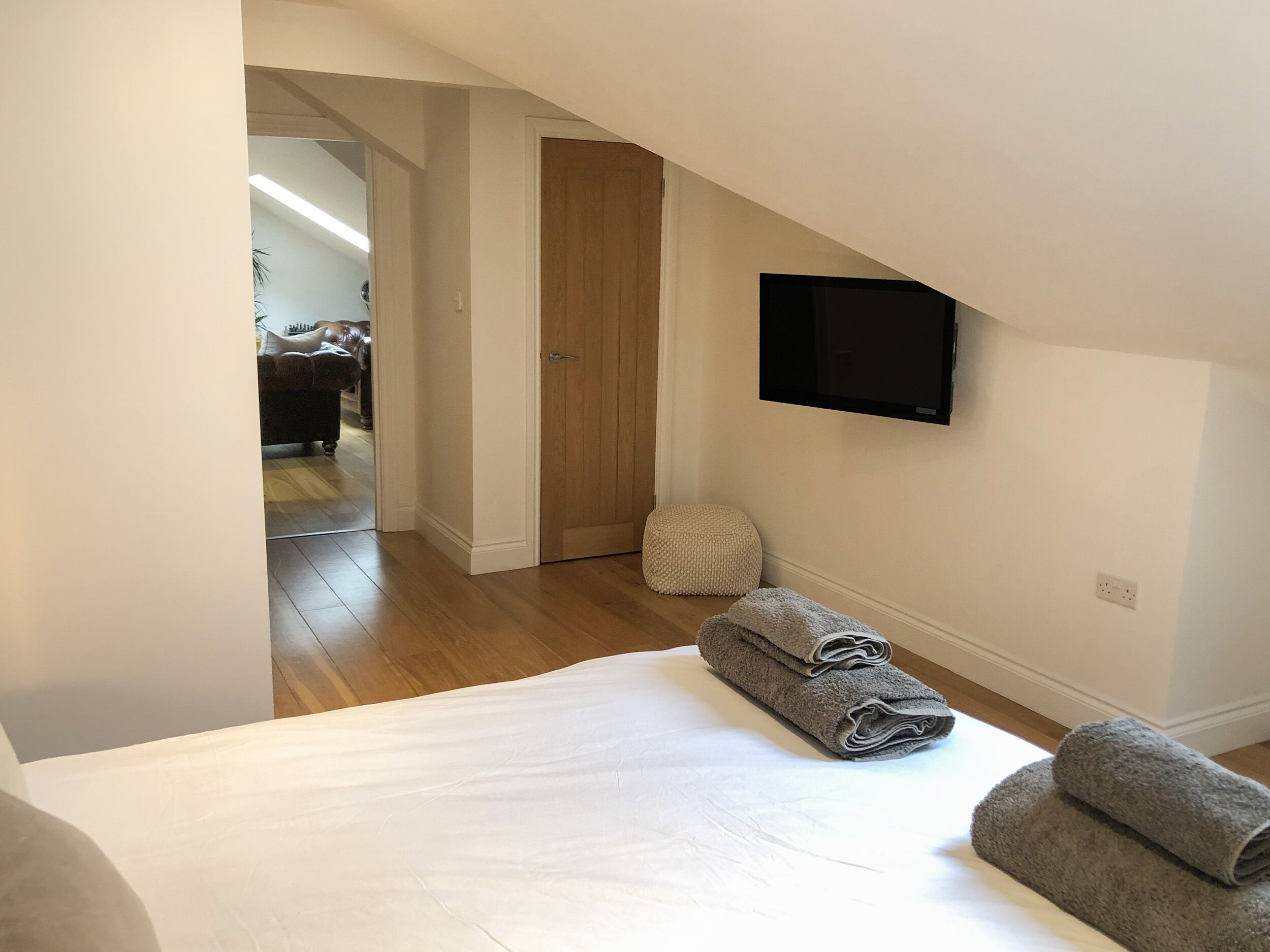 A bedroom with a bed, a TV mounted on the wall, a wooden door, and a hallway leading to another room.