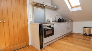 A modern kitchen with wooden flooring, white cabinetry, a built-in oven, and a skylight. - The Hideaway (St Ives)