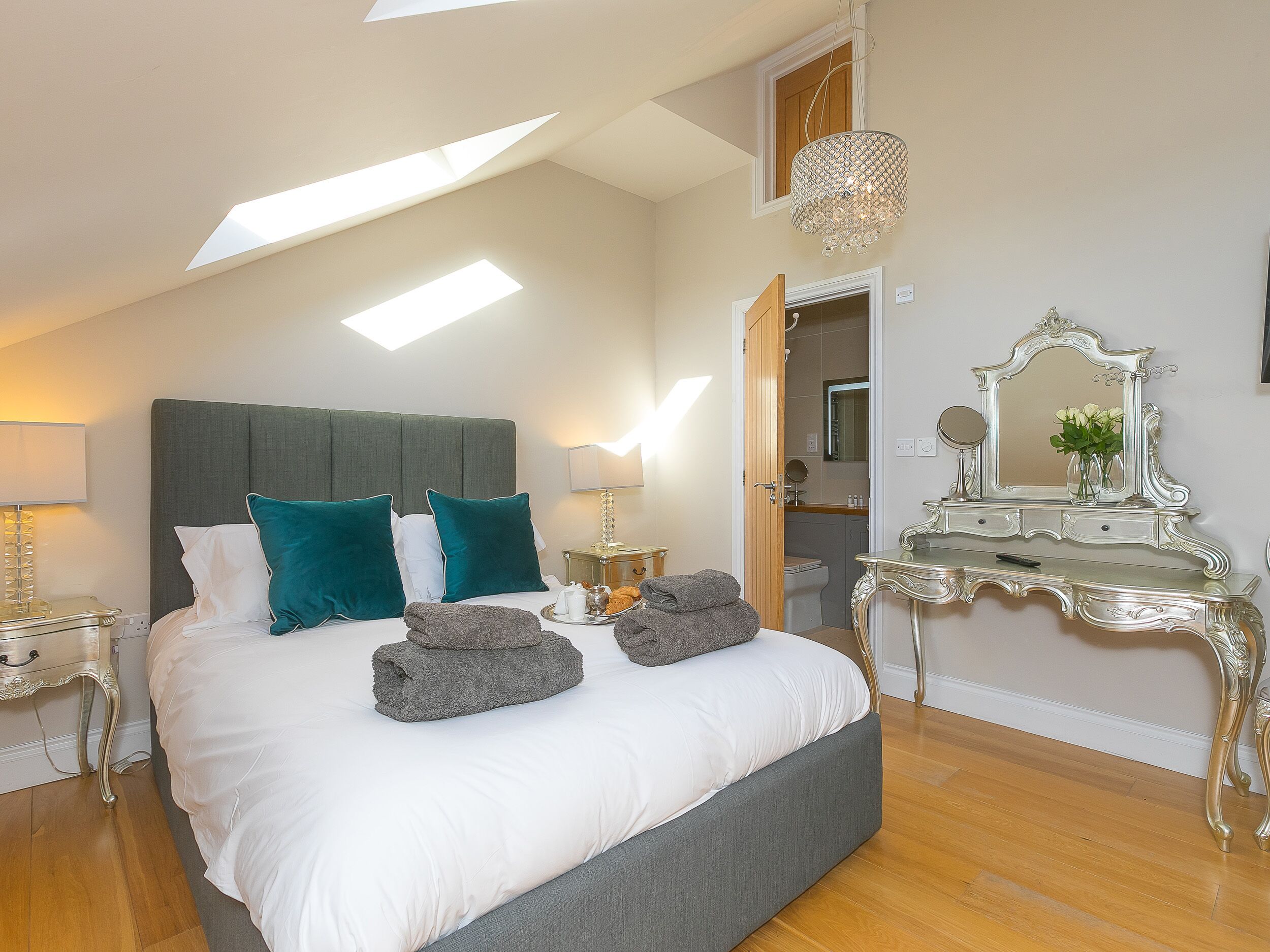 A bedroom with a large bed, a vanity with a mirror, and a skylight.