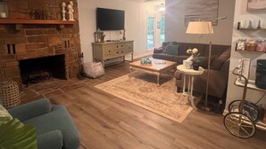 A living room with a stone fireplace, a television, a sofa, a coffee table, and a lamp. - The Hangout- Comfy Getaway in the Woods (Hot Springs)
