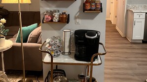 A cozy living room with a coffee station, a lamp, and a painting on the wall. - The Hangout- Comfy Getaway in the Woods (Hot Springs)