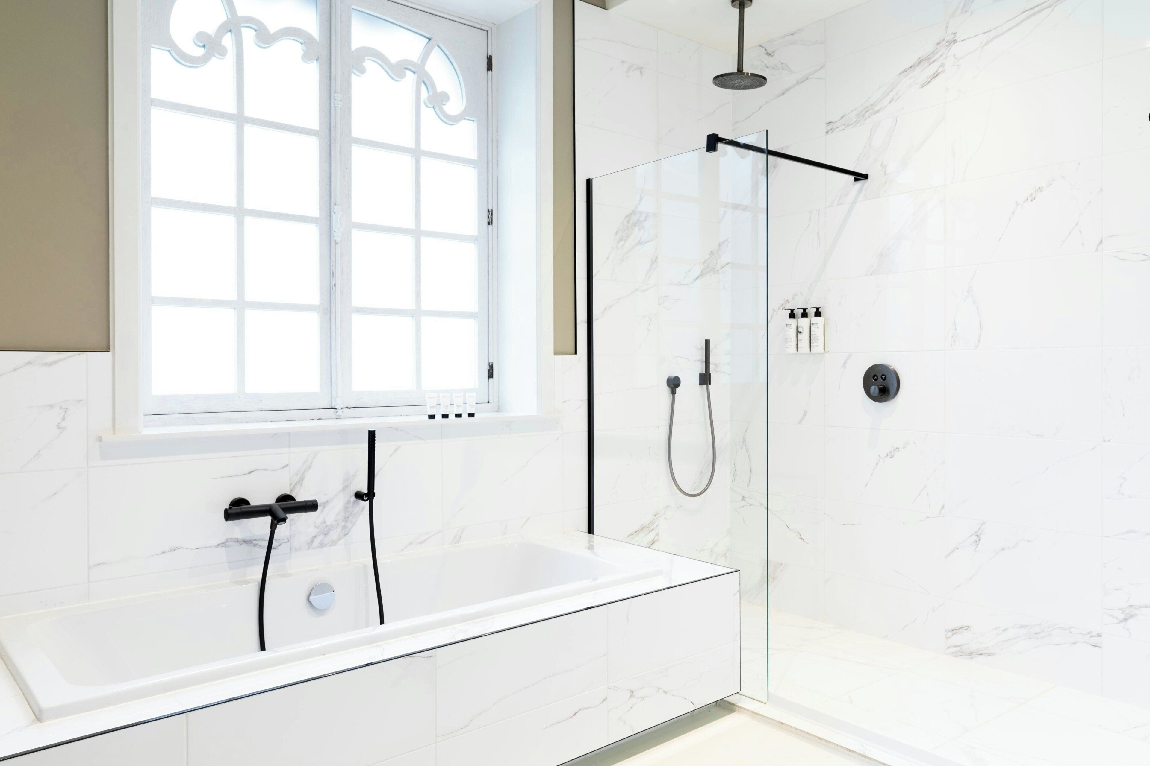 Een moderne badkamer met een douchecabine van glas, een vrijstaand bad en een raam met decoratief glas.