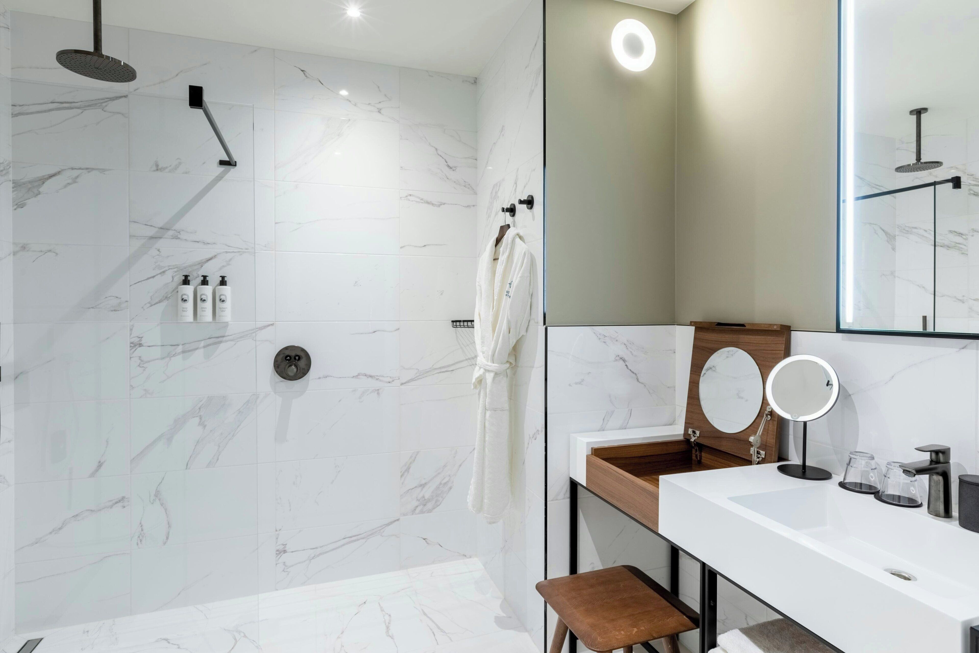 A modern bathroom with a white marble shower, a large mirror, and a wooden vanity.