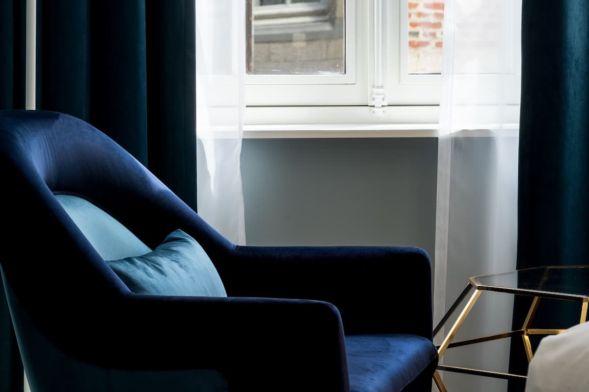A room with a dark blue armchair, a modern floor lamp, and a window with a view of a brick building.