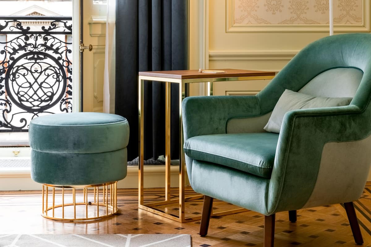 A room with a green armchair, a matching ottoman, a floor lamp, and a patterned wall.