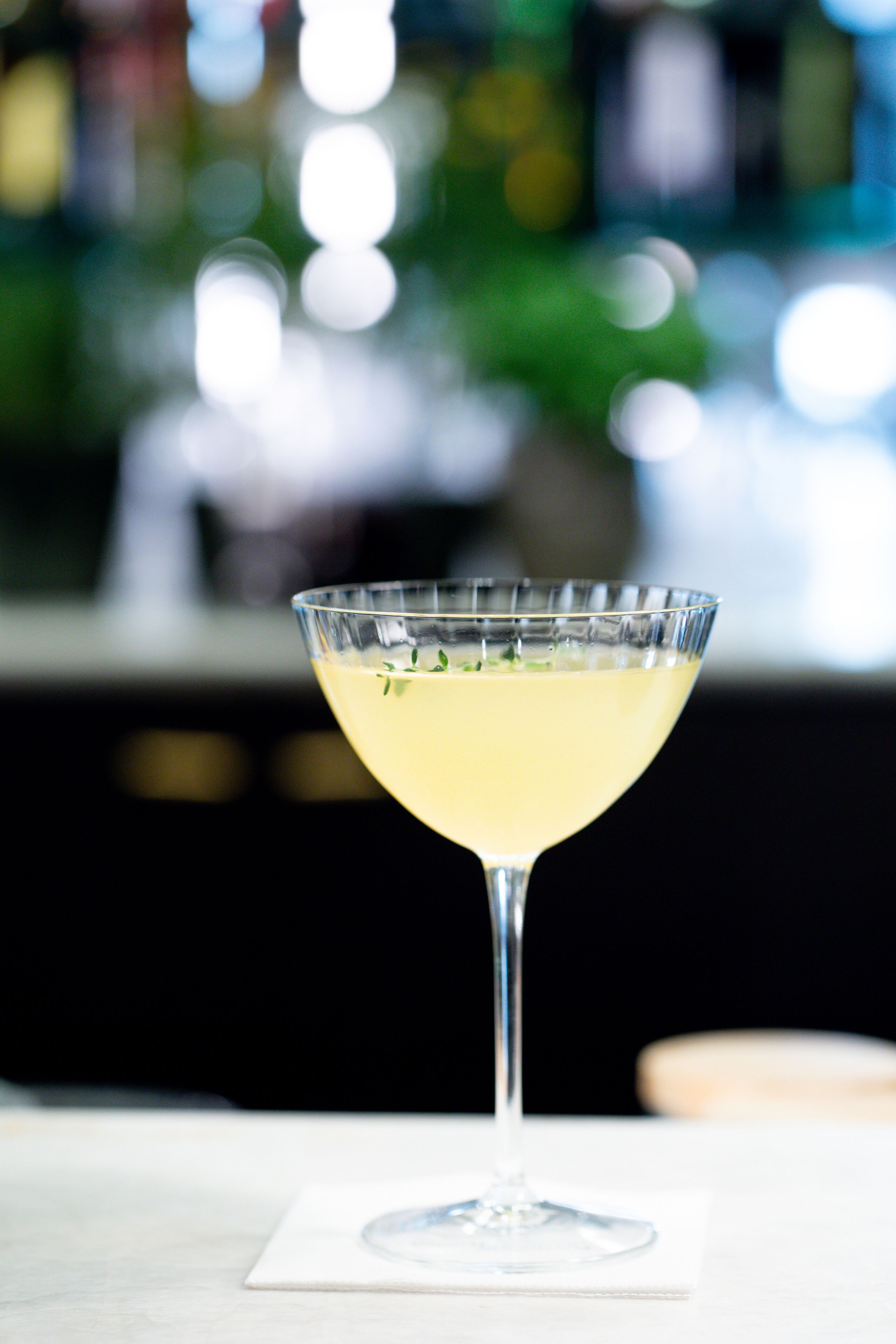 Een cocktail in een martini-glas op een witte onderzetter.