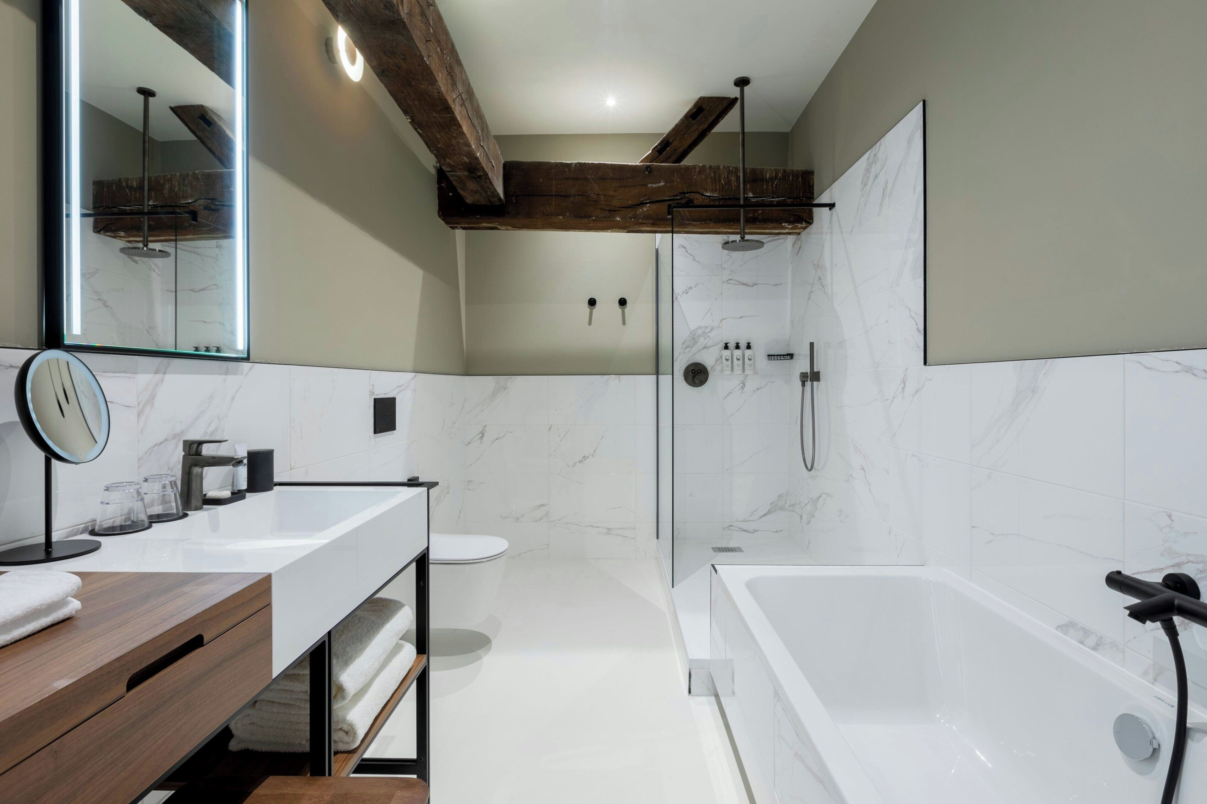 A modern bathroom with a large mirror, a wooden vanity, a bathtub, and a glass-enclosed shower.
