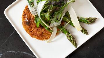 Un plato blanco con un guiso de tortitas de patata crujientes, espárragos y una guarnición de verduras de hoja.