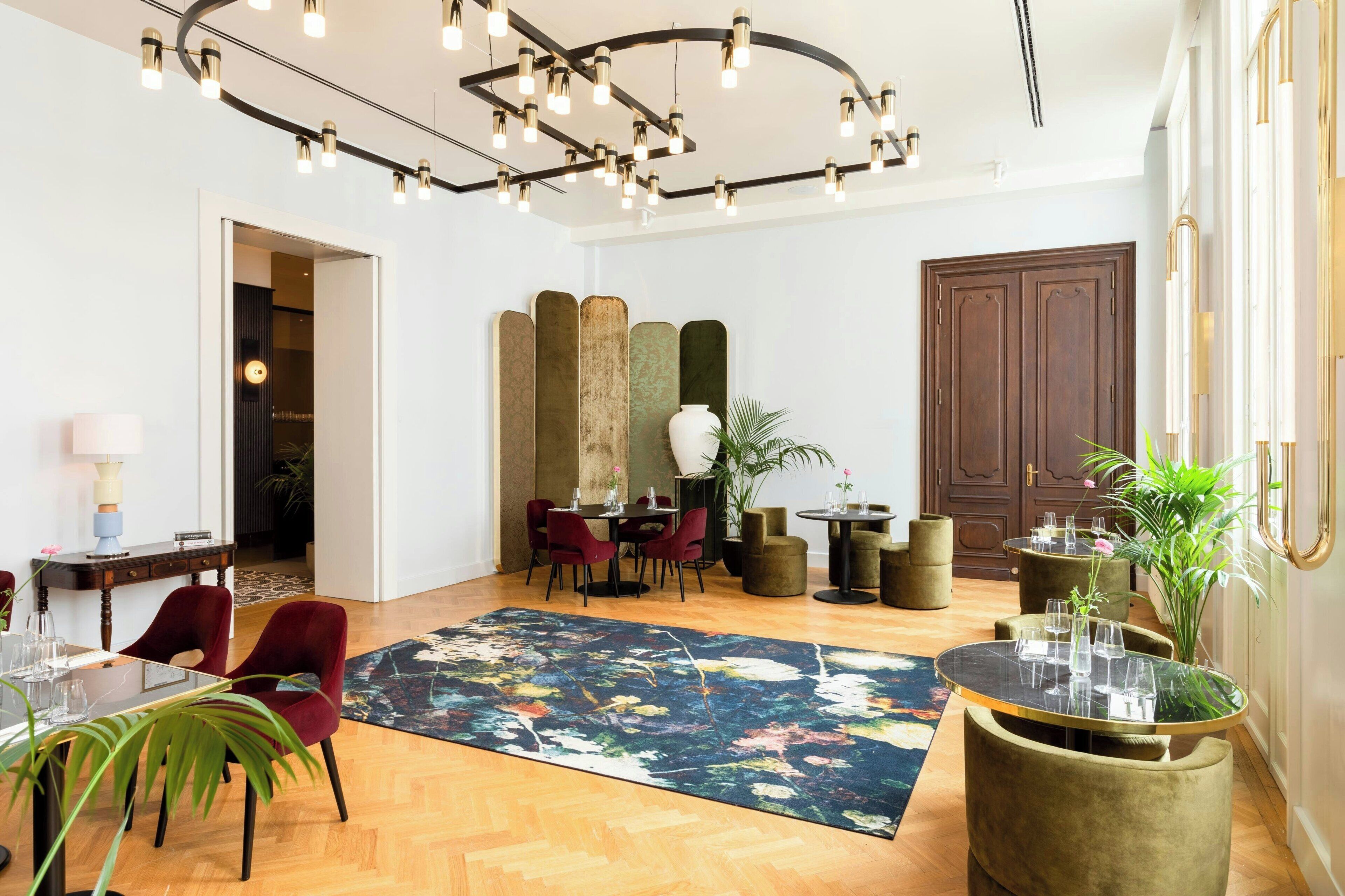 Un vaste espace de vie doté d’un plancher en bois, d’un grand tapis à motifs floraux, d’une table à manger avec des chaises et d’un coin salon comprenant un canapé et une table basse.