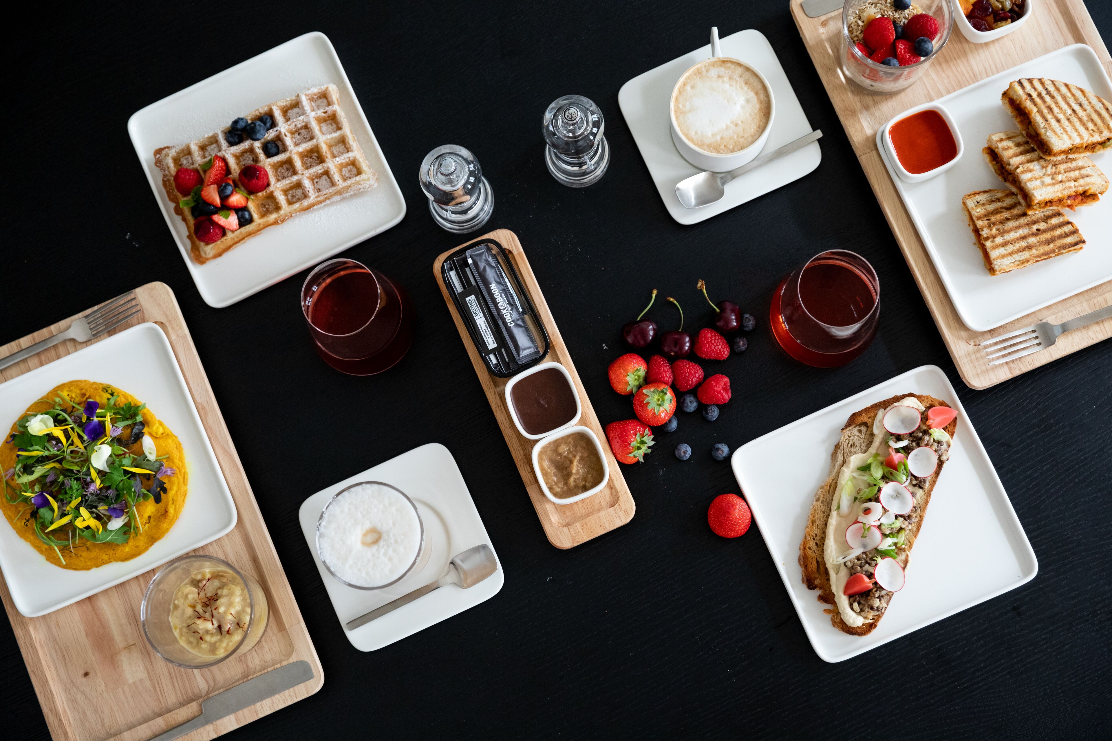 Un assortiment de mets pour le petit-déjeuner, comprenant des gaufres, des toasts et divers fruits, disposés sur une table noire.
