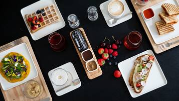 Un assortiment de mets pour le petit-déjeuner, comprenant des gaufres, des toasts et divers fruits, disposés sur une table noire.