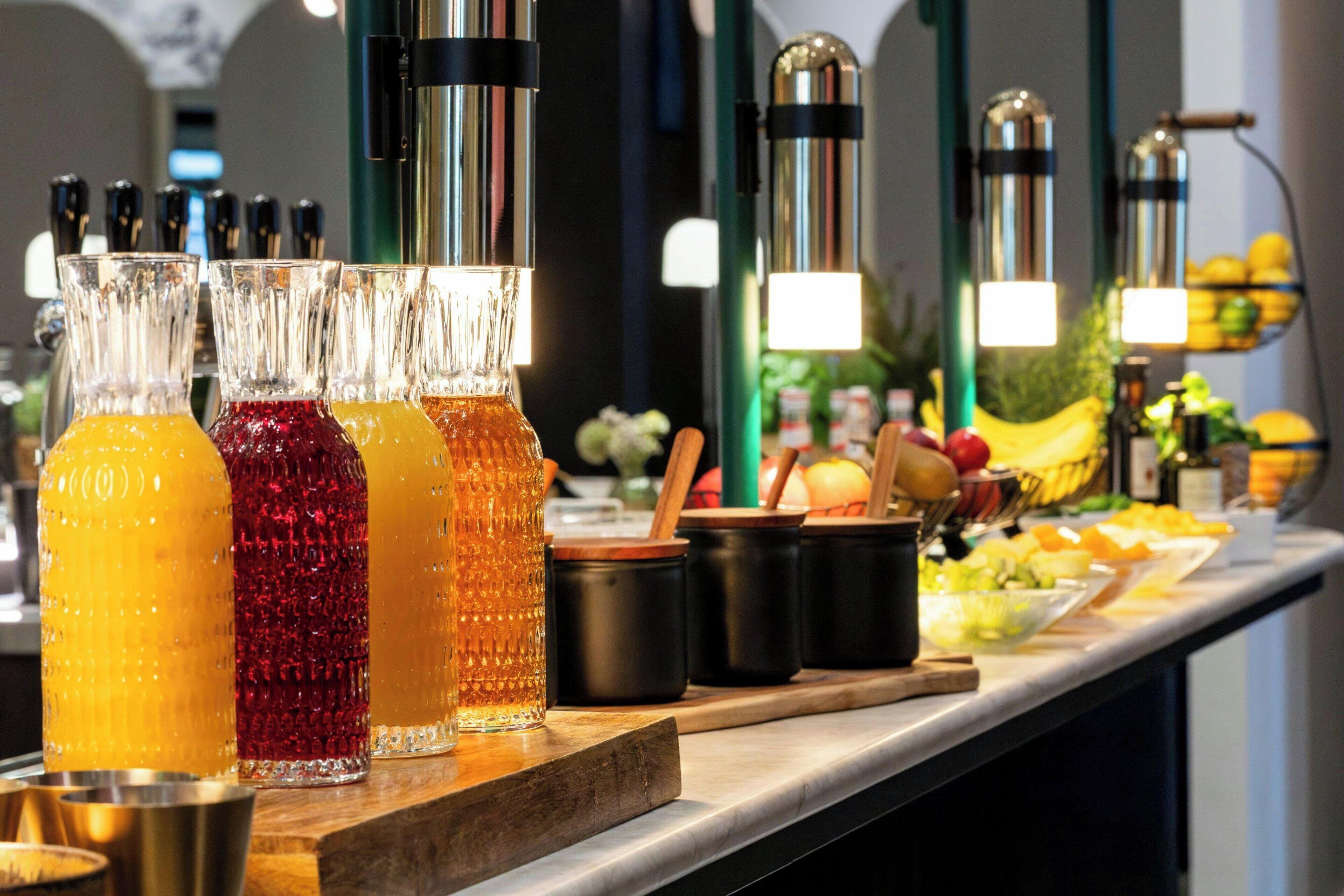 Un banco buffet con diverse bevande in bicchieri trasparenti, una varietà di frutta e utensili da cucina.
