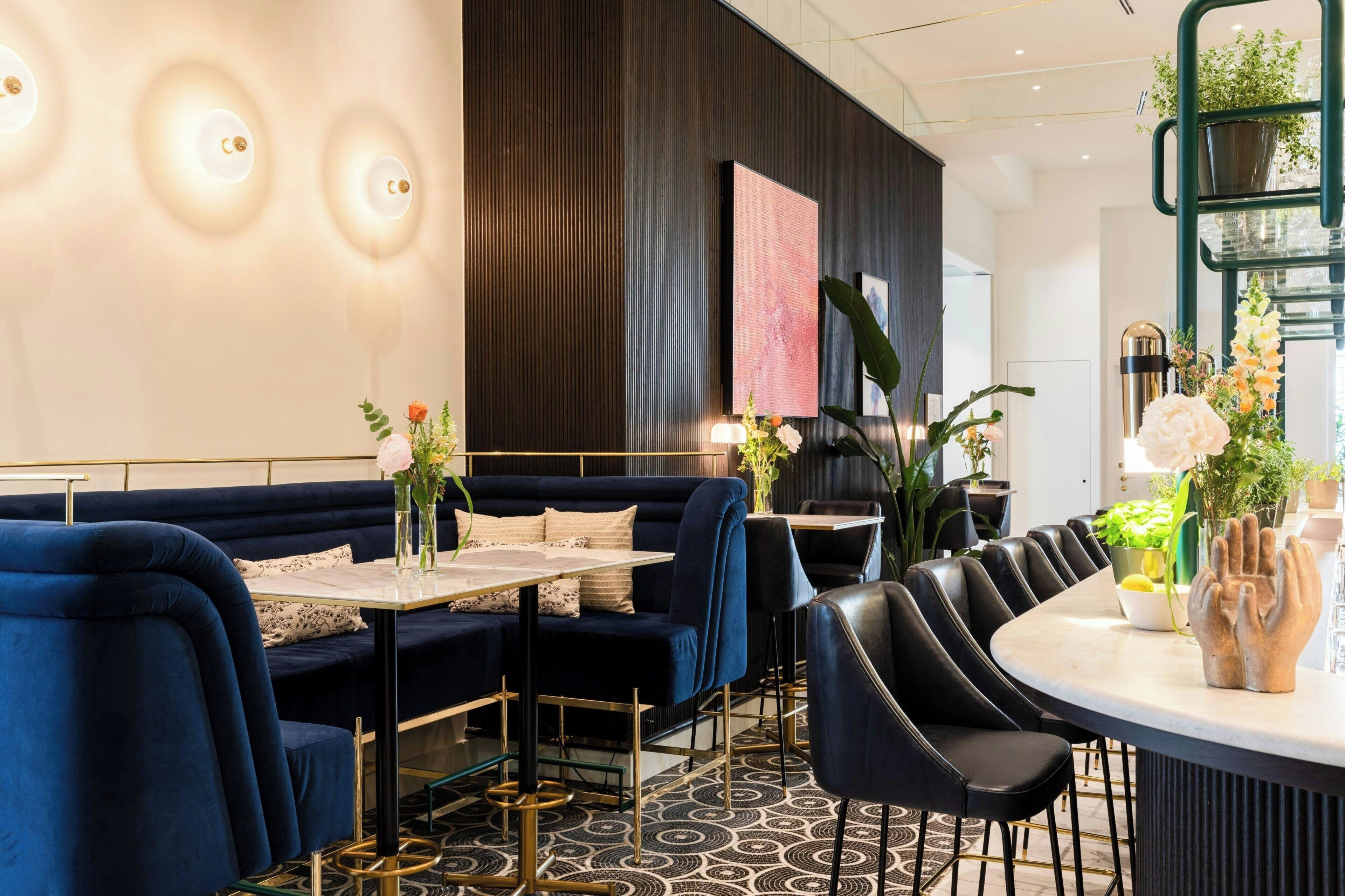 Un espace repas moderne avec un canapé bleu foncé, des chaises noires, une table ronde et un arrangement floral décoratif en guise de centre de table.