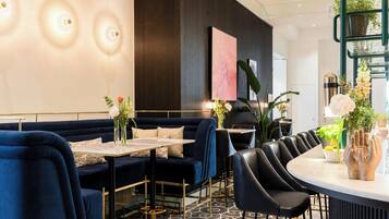 Un espace repas moderne avec un canapé bleu foncé, des chaises noires, une table ronde et un arrangement floral décoratif en guise de centre de table.