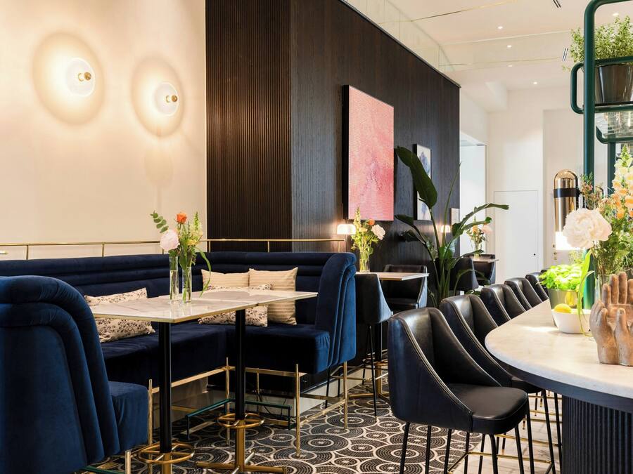 Un espace repas moderne avec un canapé bleu foncé, des chaises noires, une table ronde et un arrangement floral décoratif en guise de centre de table.
