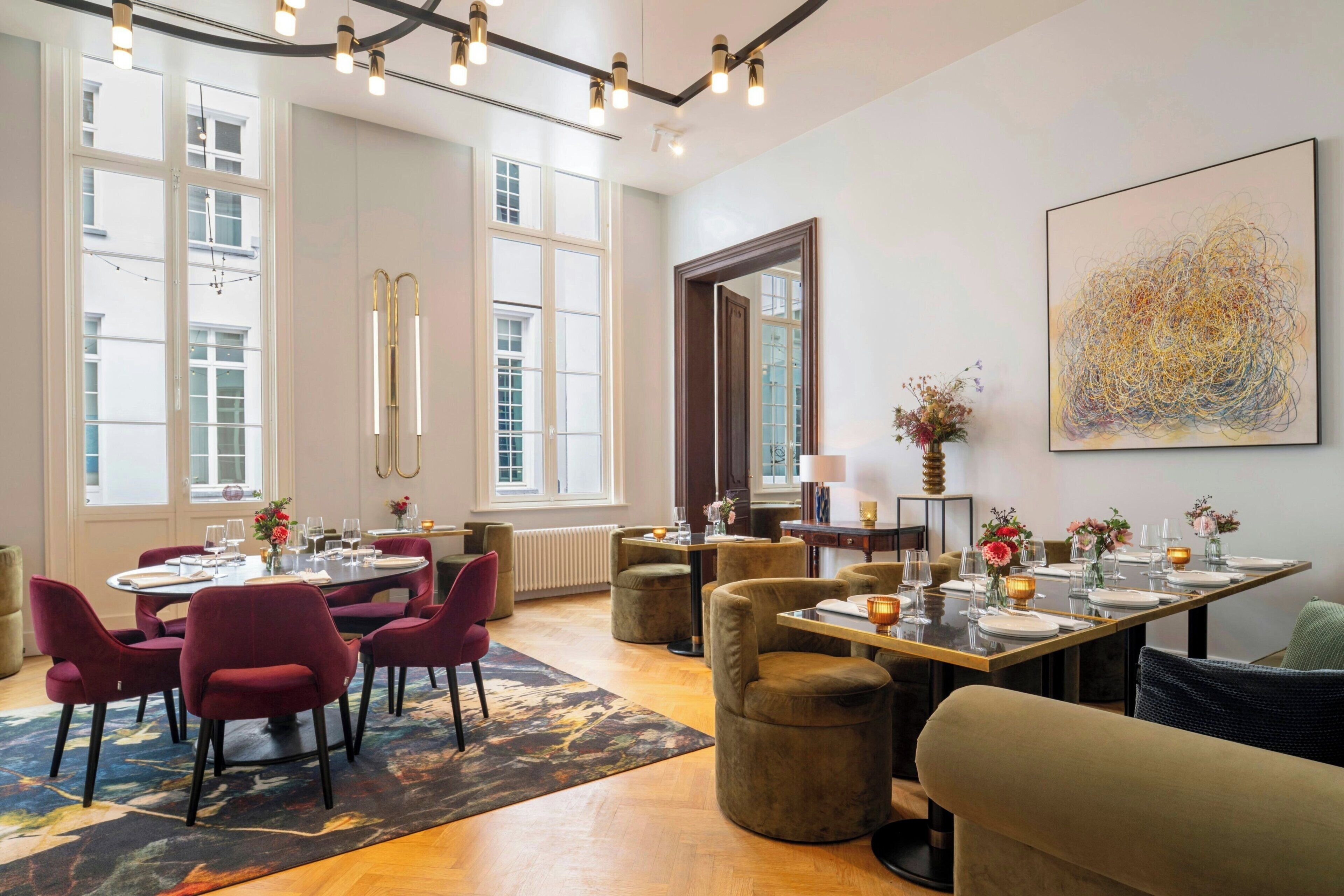 A dining area with round tables, red chairs, and a large abstract painting on the wall.