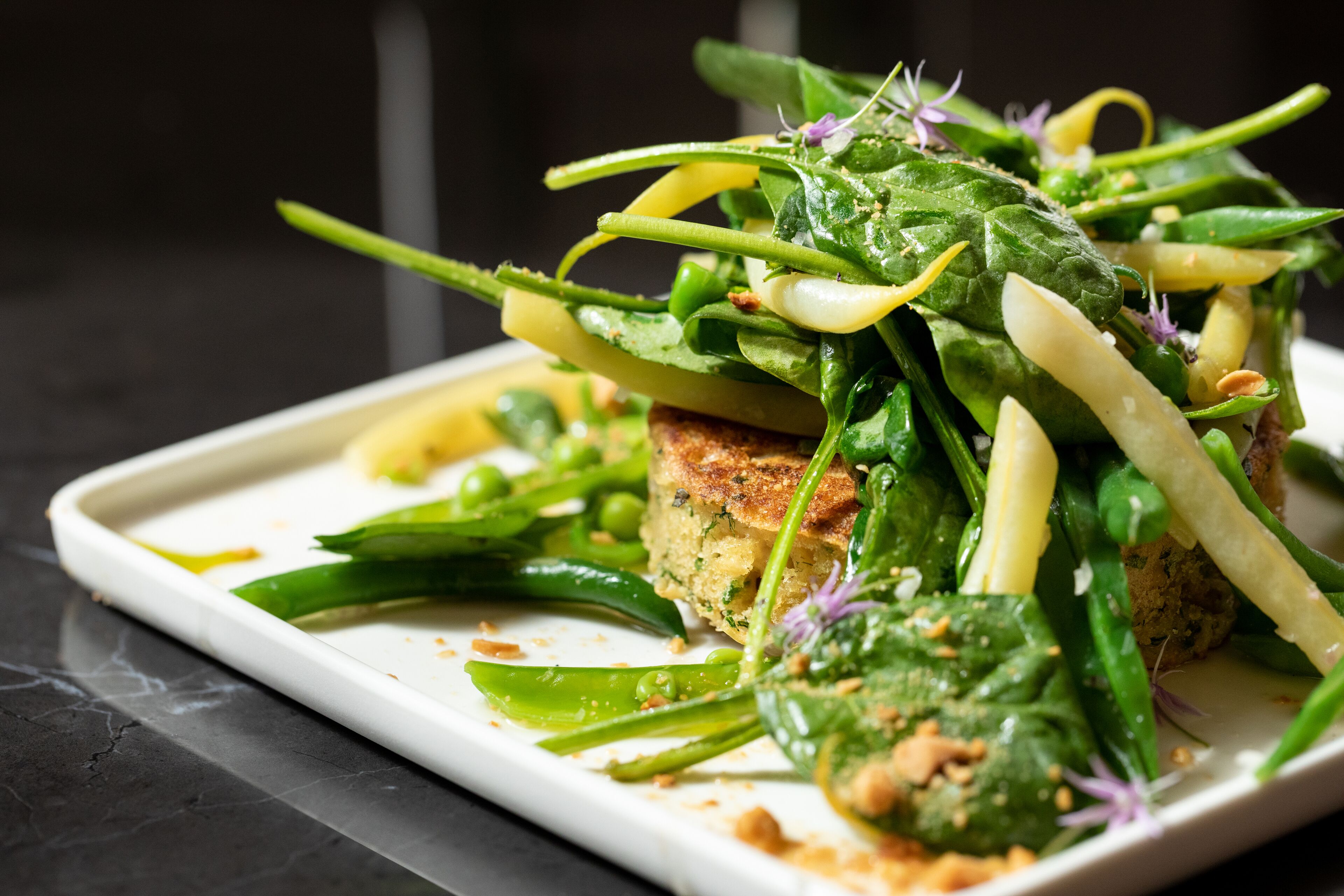 A rectangular white plate with a variety of green vegetables and a piece of bread.