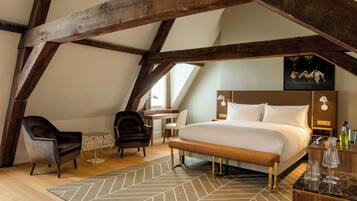 A bedroom with a large bed, wooden beams, a desk, two chairs, and a small table with a lamp.