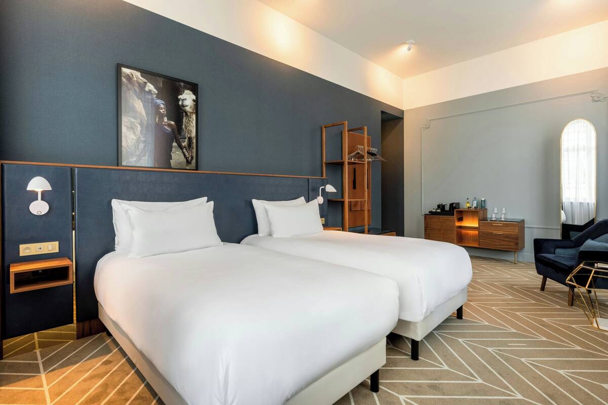 Ein Hotelzimmer mit zwei Betten, einem Kleiderschrank, einem Schminktisch mit Spiegel und einem großen Fenster.