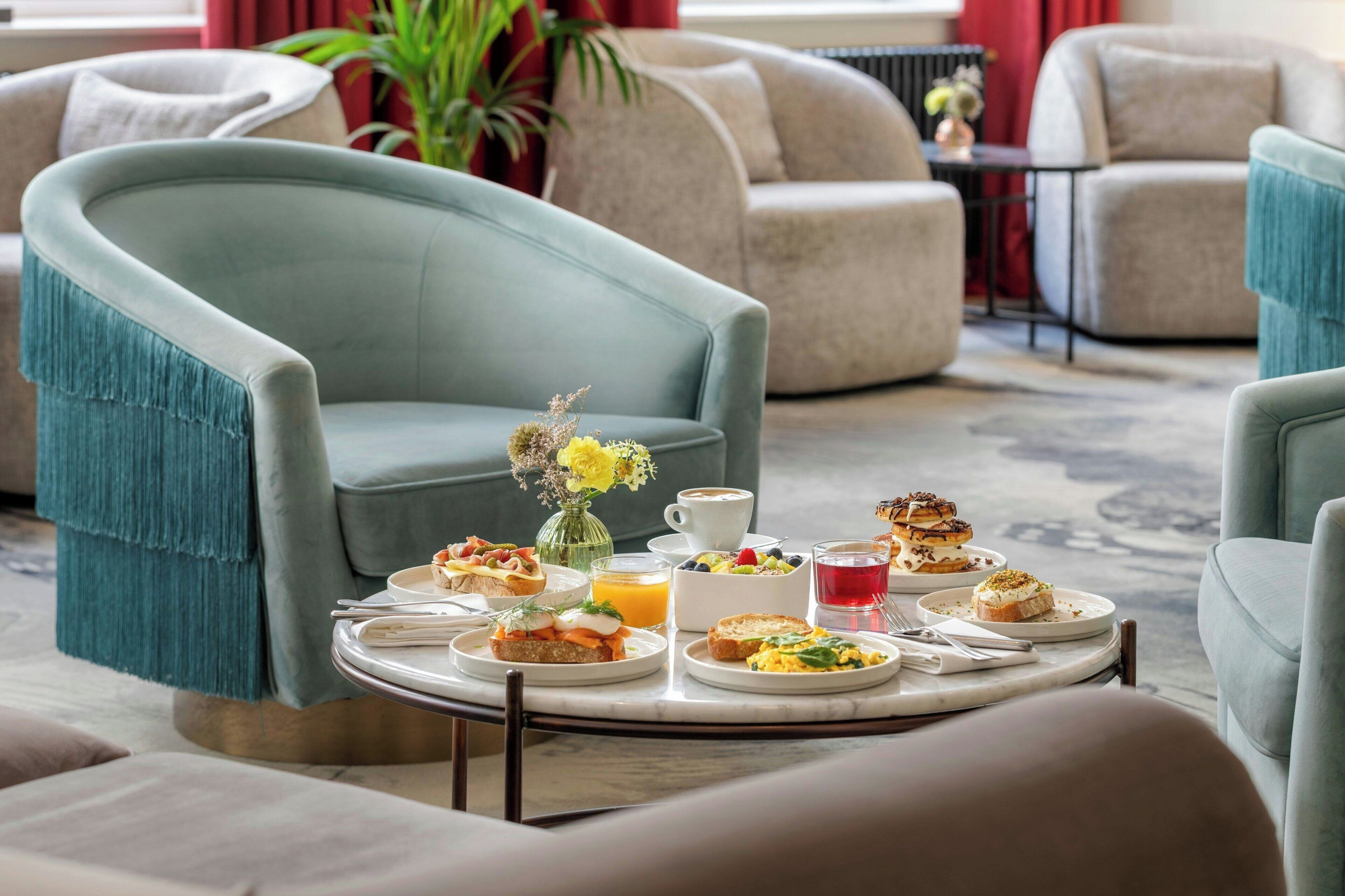 A dining area with a round table set with various breakfast items, surrounded by comfortable seating.