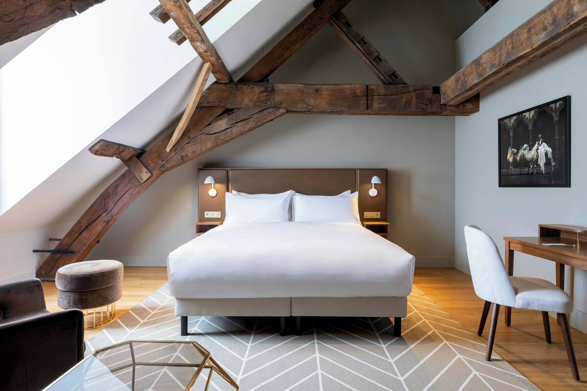 Ein modernes Schlafzimmer mit einem großen Bett, Holzbalken, einem Schreibtisch und einem Sessel.