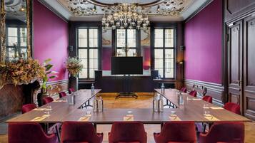 A conference room with a long table, red chairs, a chandelier, and a large mirror.