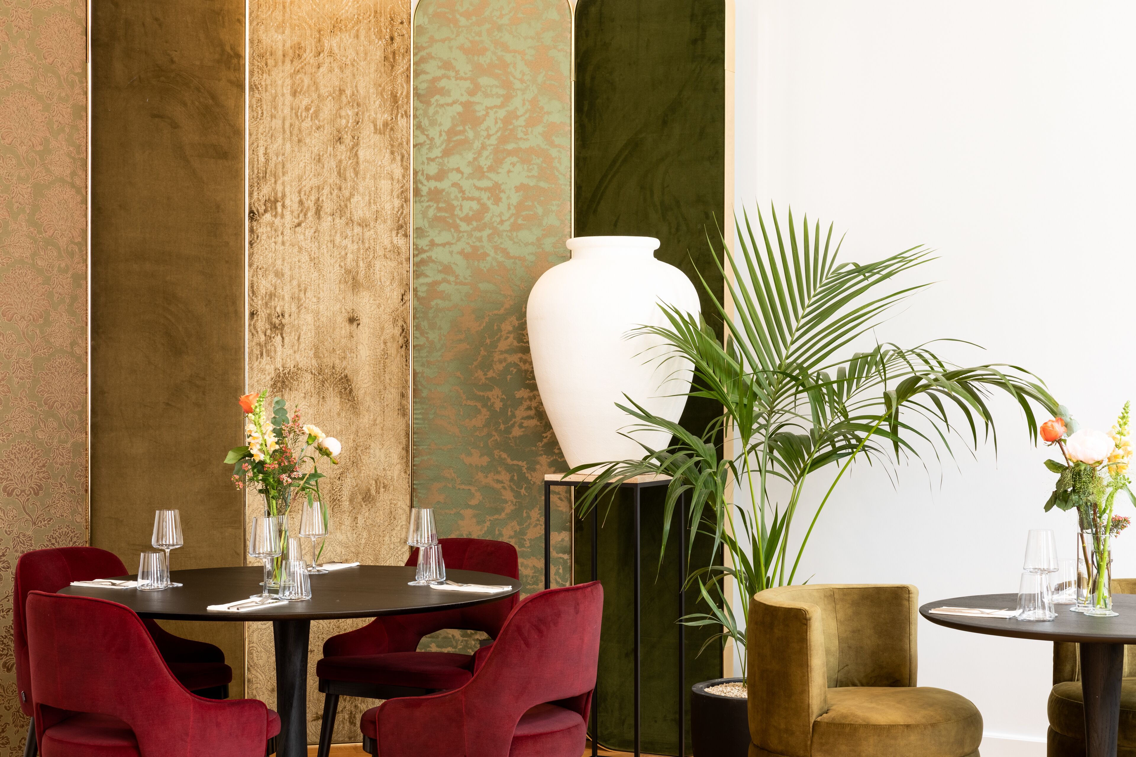 A dining area with a table set for four, surrounded by red chairs, with a large white vase and a potted plant on the table.