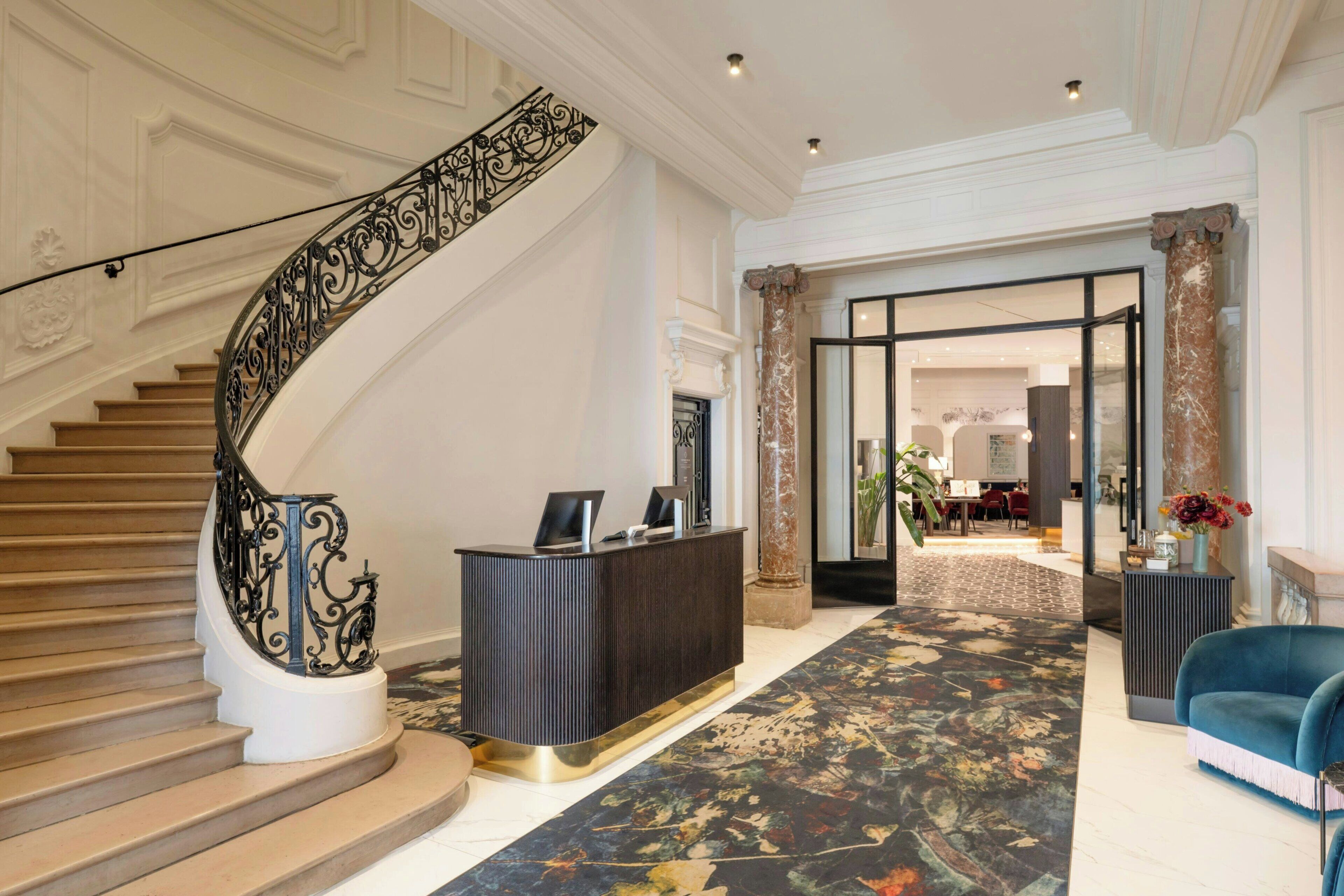 A grand lobby with a curved staircase, a reception desk, and a blue armchair.