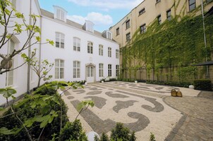 Un cortile con pavimento in pietra decorato, circondato da edifici dalle facciate bianche e beige, alcuni ricoperti d'edera.