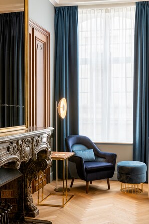 A room with a dark blue armchair, a matching ottoman, and a marble fireplace. - Sapphire House Antwerp, Autograph Collection (Antwerp)