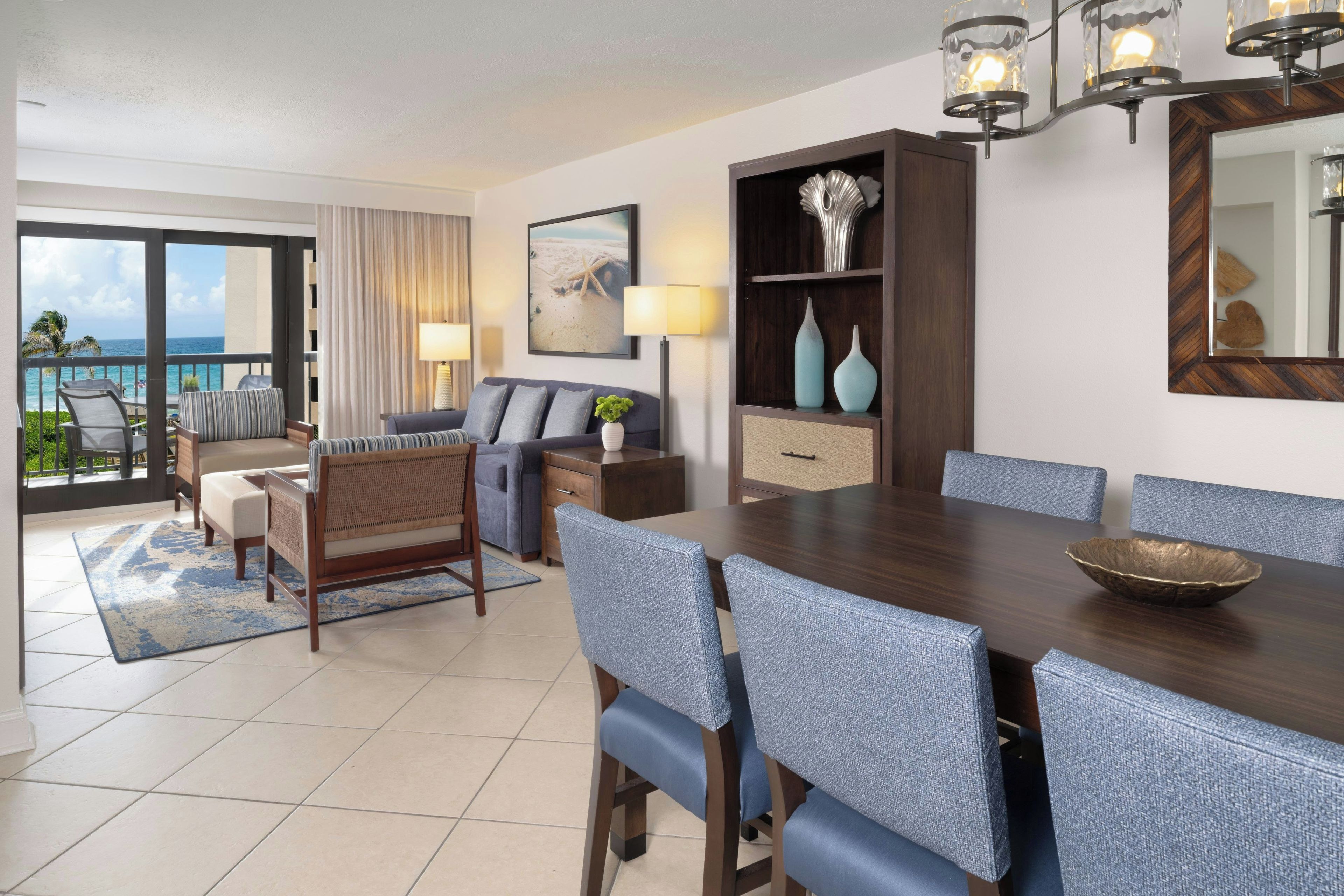 A hotel room with a balcony, a dining area, and a living space.
