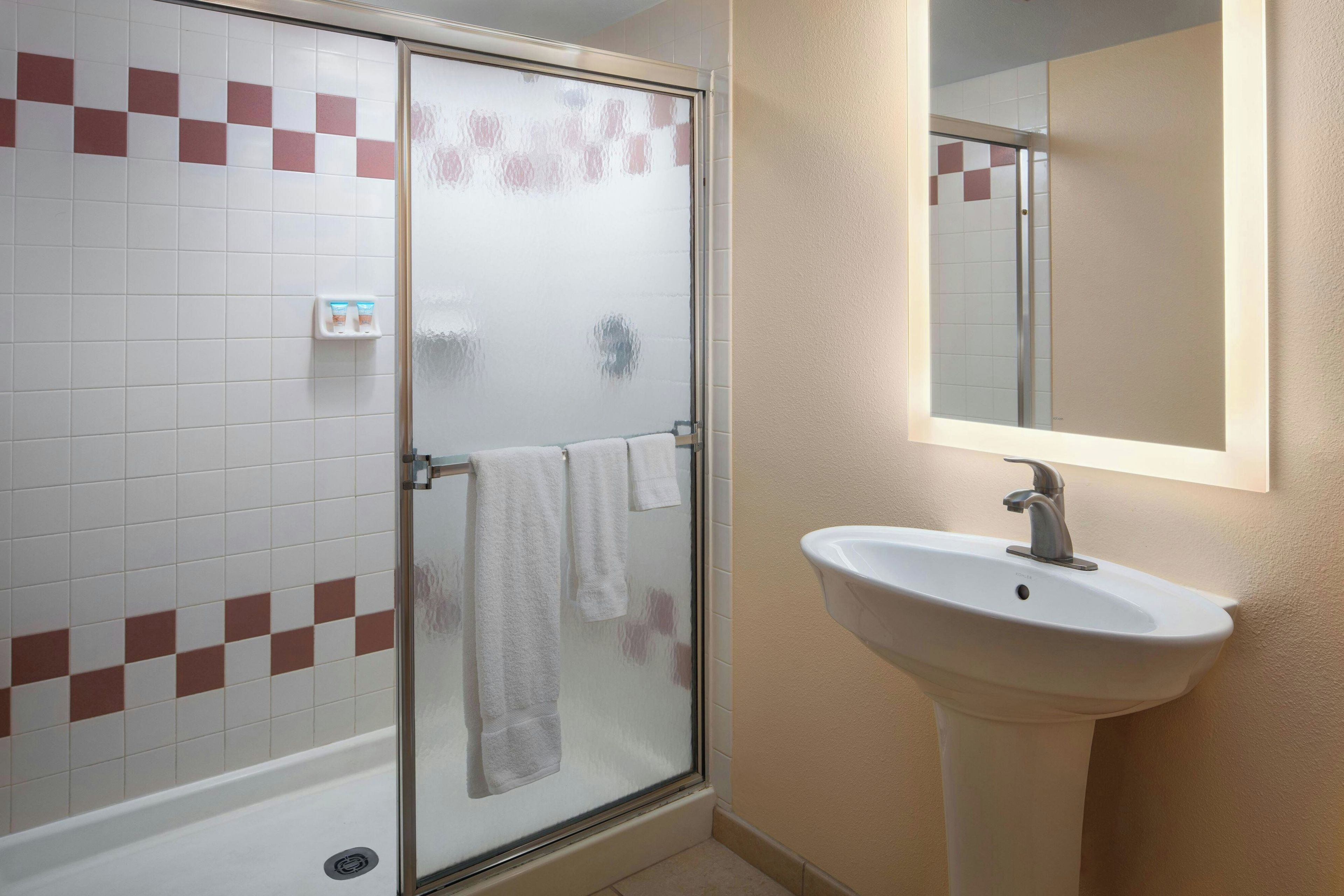Un baño con cabina de ducha de vidrio, un lavabo blanco y un espejo encima.