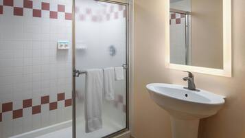 Un baño con cabina de ducha de vidrio, un lavabo blanco y un espejo encima.