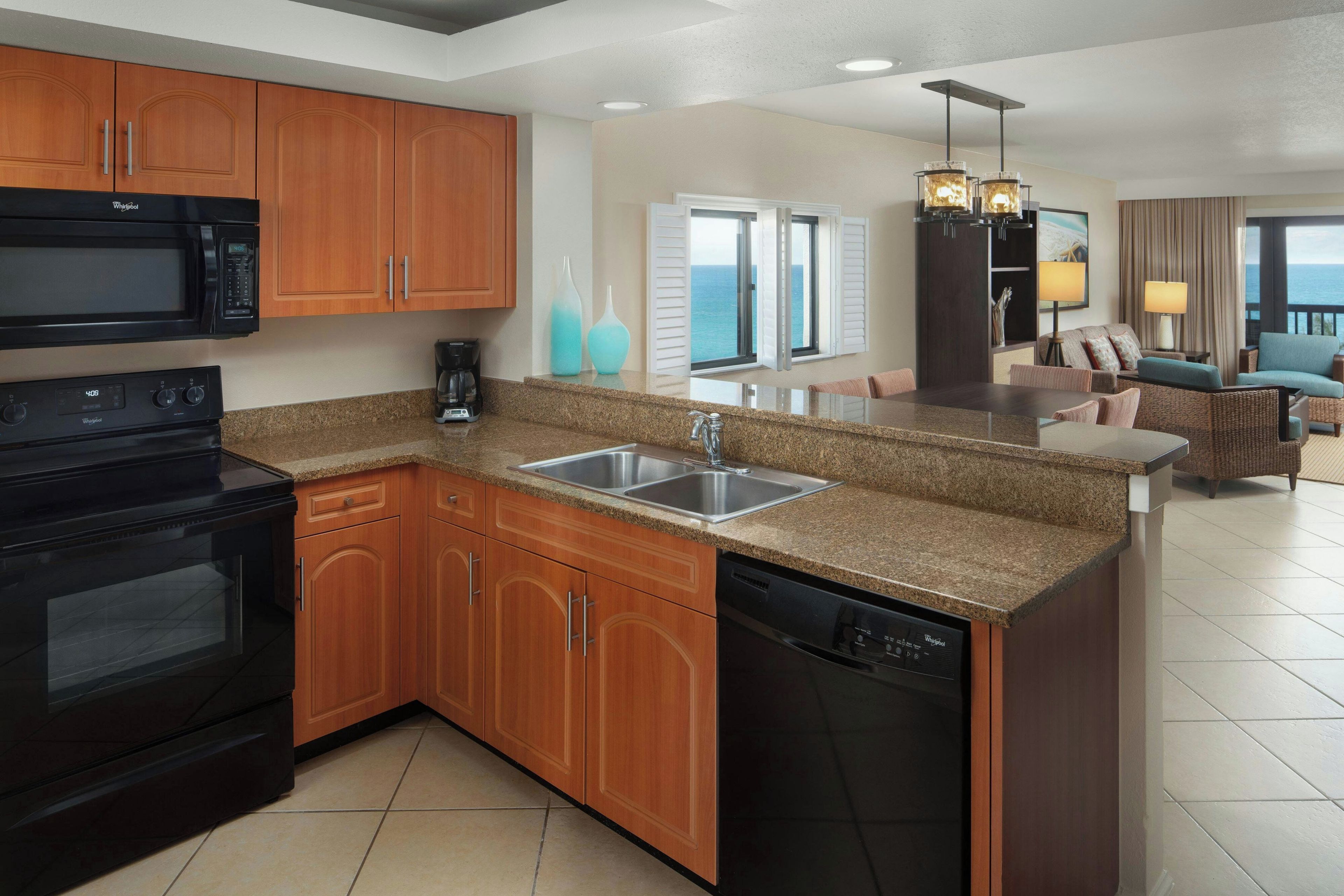 A modern kitchen with a built-in microwave, stove, and dishwasher. There is a large island with a sink and a dining area with a view of the ocean.