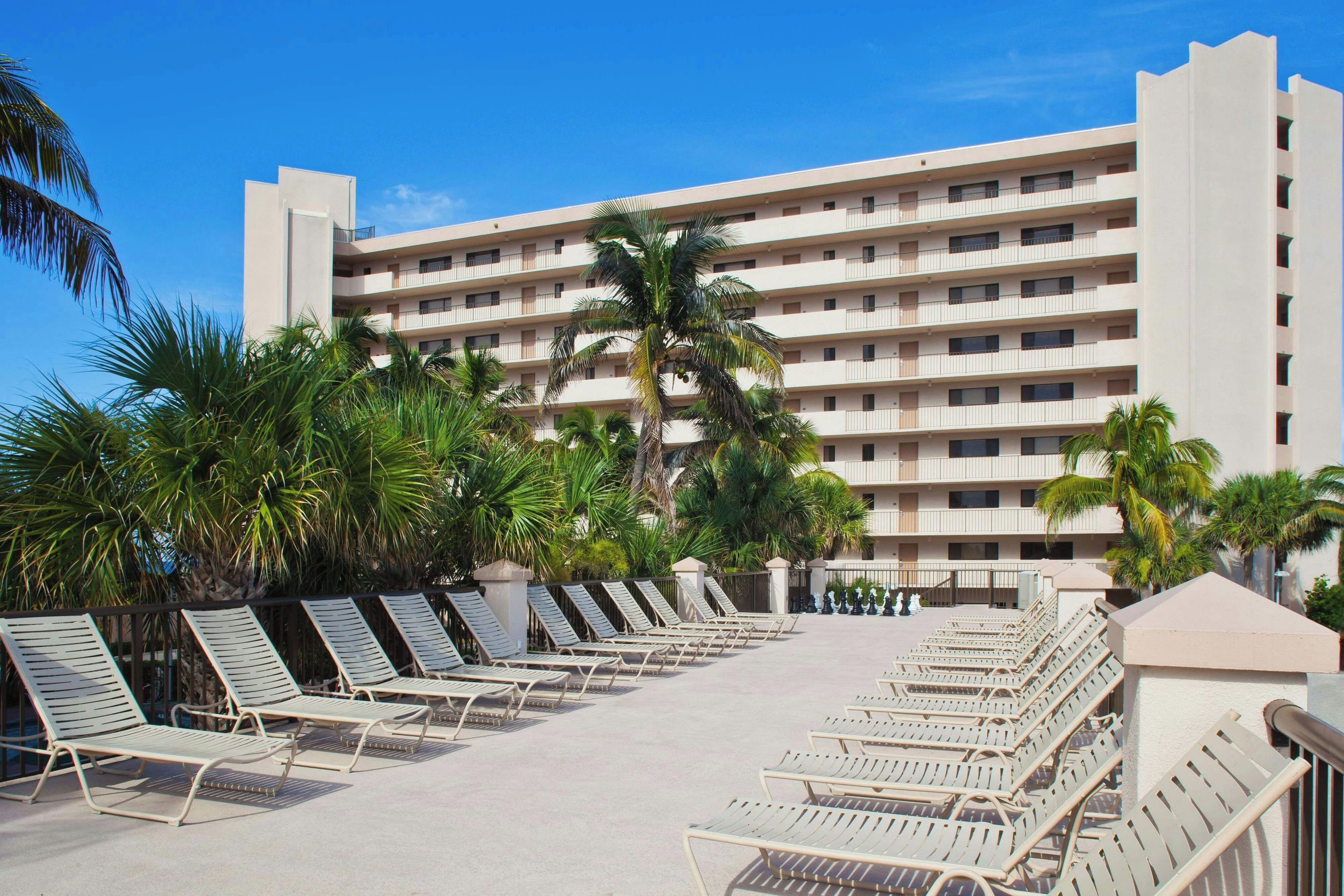 A hotel with multiple floors, outdoor pool area with lounge chairs, and palm trees.