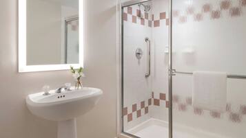 Un baño con cabina de ducha acristalada, un lavabo blanco con un florero y un espejo sobre el lavabo.