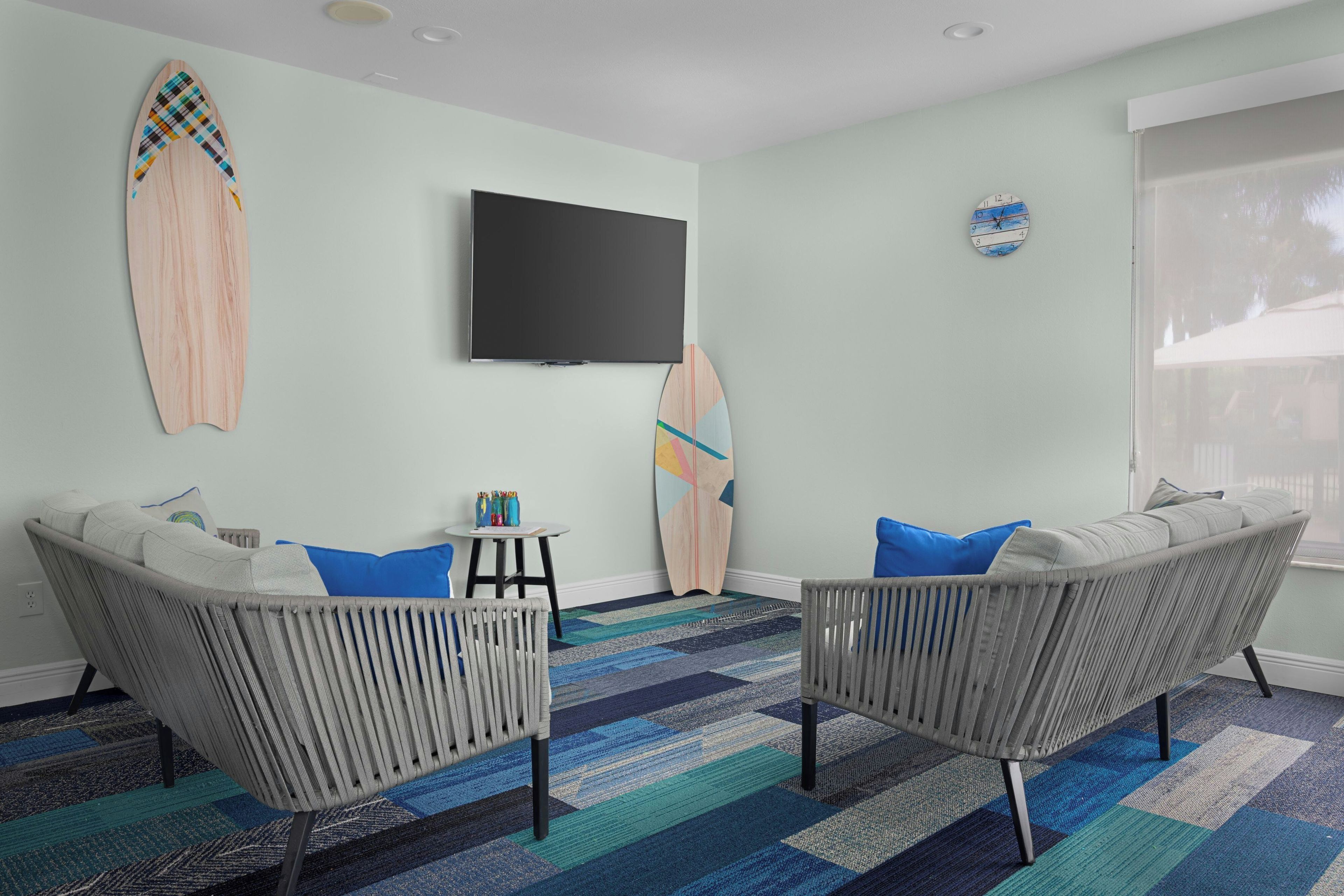 Un salon avec deux canapés gris, un téléviseur à écran plat fixé au mur et une décoration sur le thème du surf.