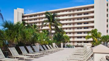 A hotel with multiple floors, a pool area with sun loungers, and palm trees.