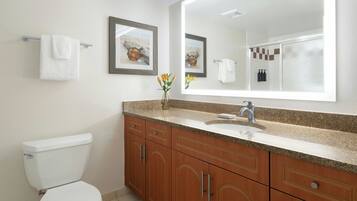 A bathroom with a toilet, a sink, and a mirror. There are towels on the wall and a vase with flowers on the counter.