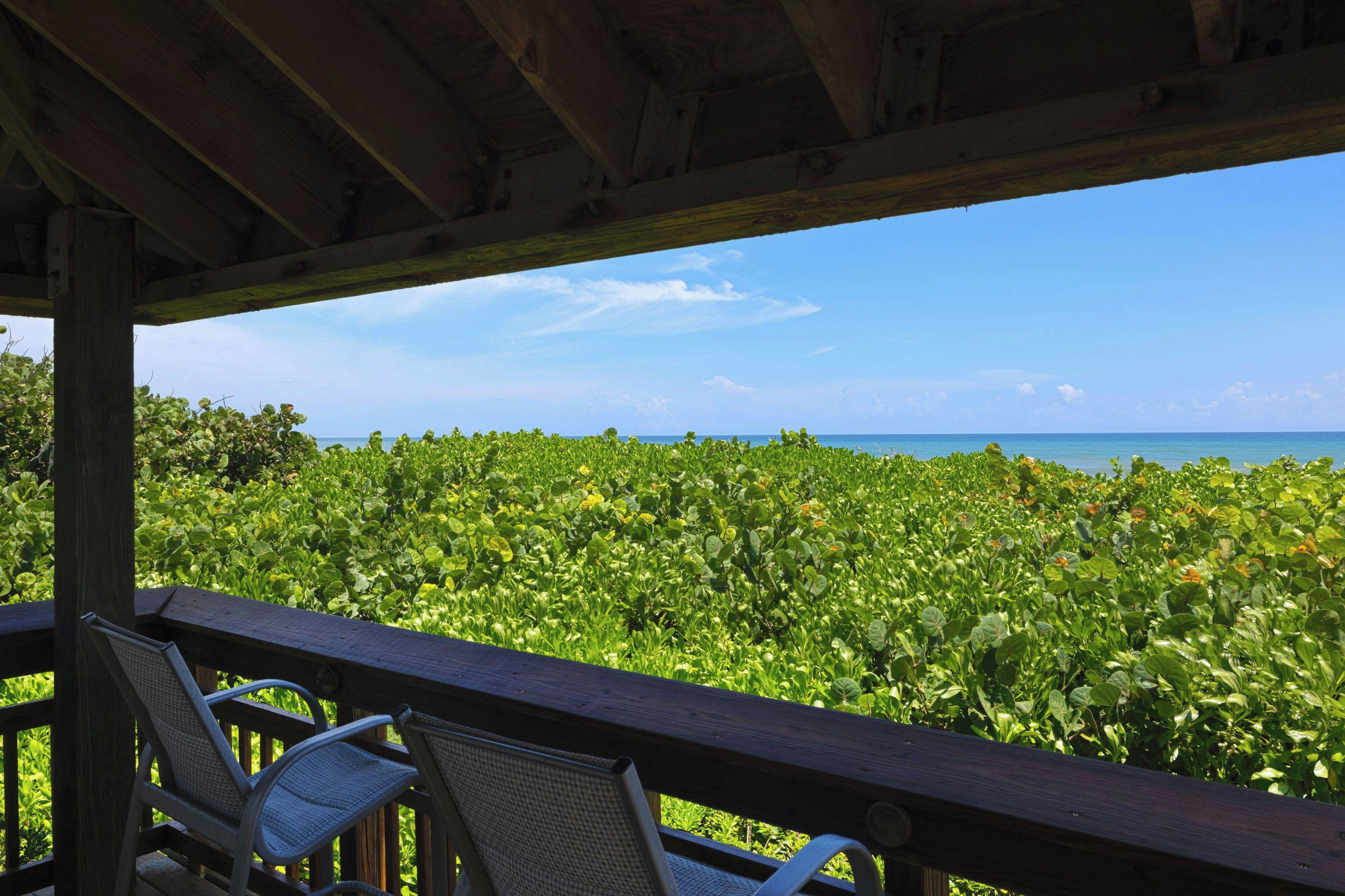 A wooden deck with chairs overlooking a lush green landscape and a clear blue sky.